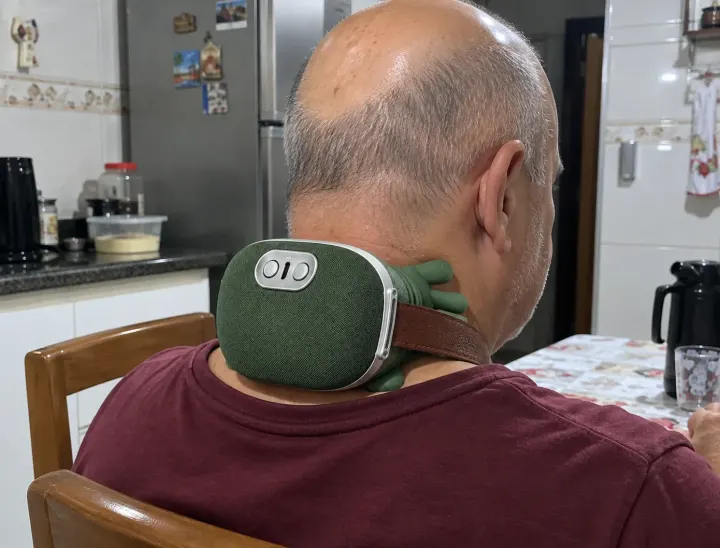 Homem sentado na cozinha com o massageador na nuca